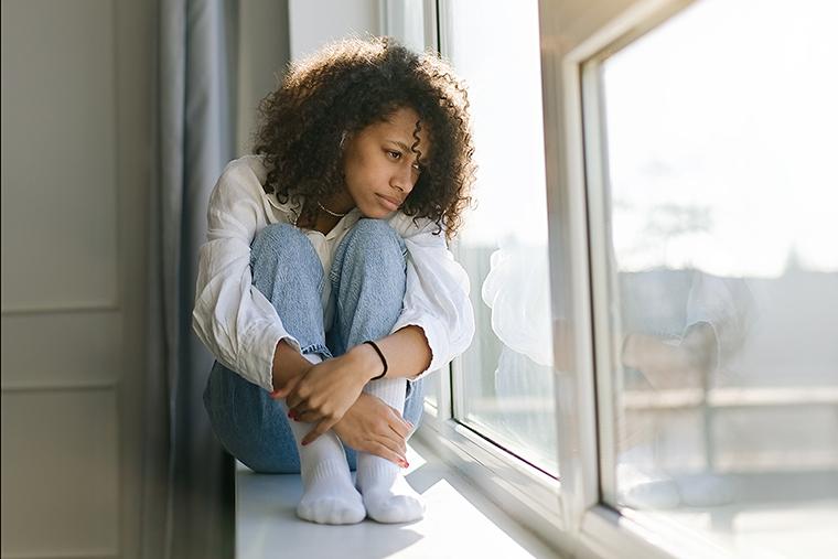 Mulher reflexiva diante da janela, pensando sobre o futuro e a incerteza.